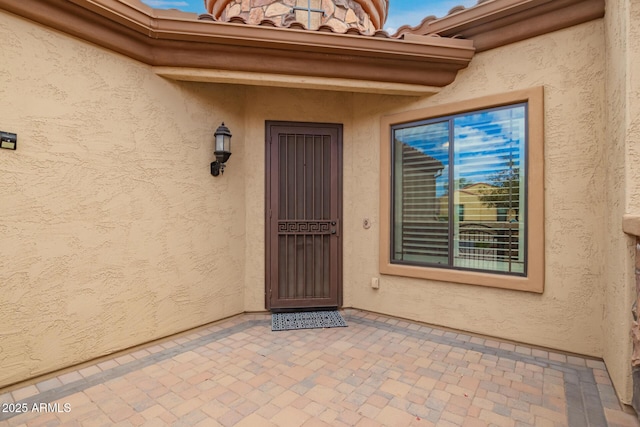 view of exterior entry with stucco siding and a tiled roof