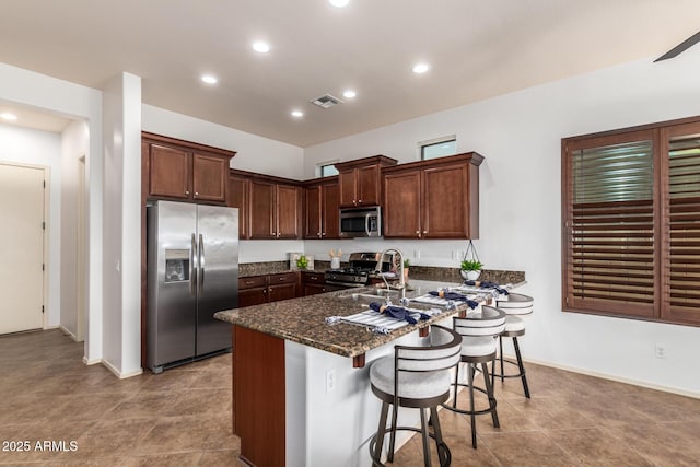 kitchen with visible vents, a sink, stainless steel appliances, dark stone counters, and a peninsula