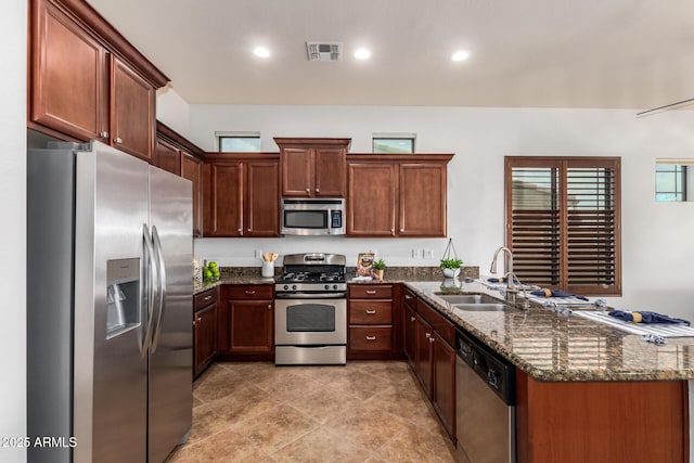 kitchen featuring visible vents, dark stone countertops, appliances with stainless steel finishes, a peninsula, and a sink