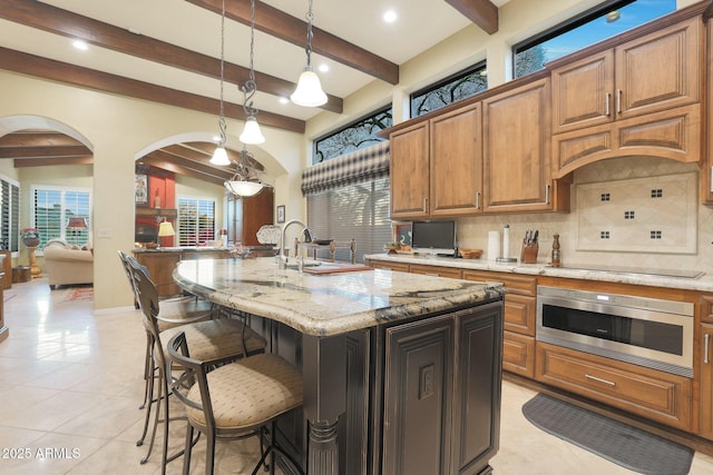 kitchen featuring light stone countertops, decorative backsplash, black electric cooktop, decorative light fixtures, and a center island with sink