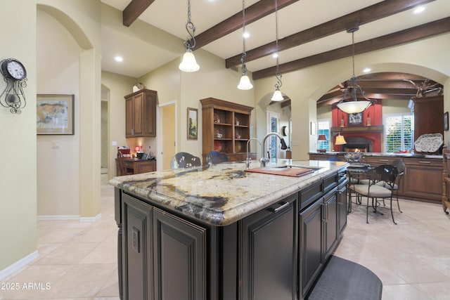 kitchen with decorative light fixtures, beam ceiling, and a kitchen island with sink