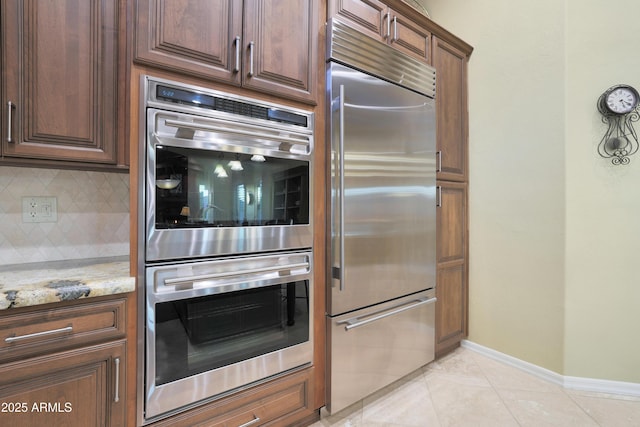 kitchen featuring decorative backsplash, stainless steel appliances, light stone counters, and light tile patterned flooring