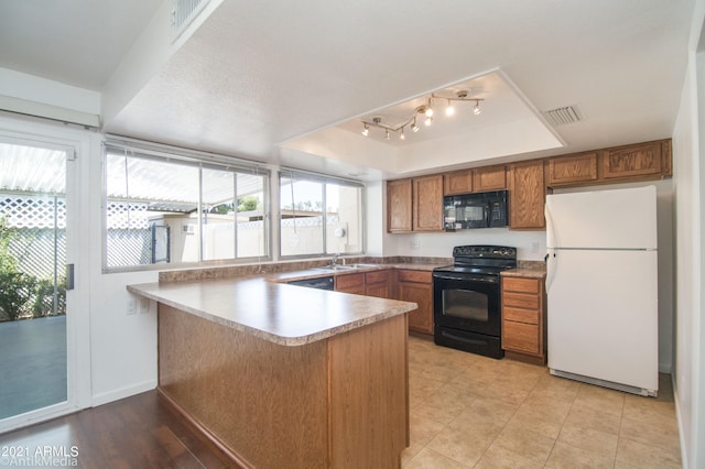 kitchen with a healthy amount of sunlight, a raised ceiling, black appliances, and kitchen peninsula