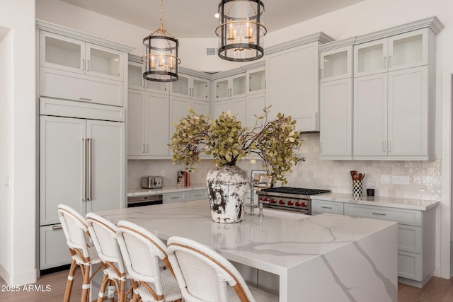 kitchen with high quality appliances, a chandelier, backsplash, light stone counters, and a kitchen island with sink