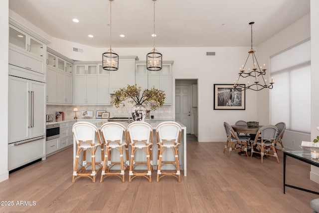 kitchen featuring paneled refrigerator, a kitchen bar, backsplash, light countertops, and a chandelier