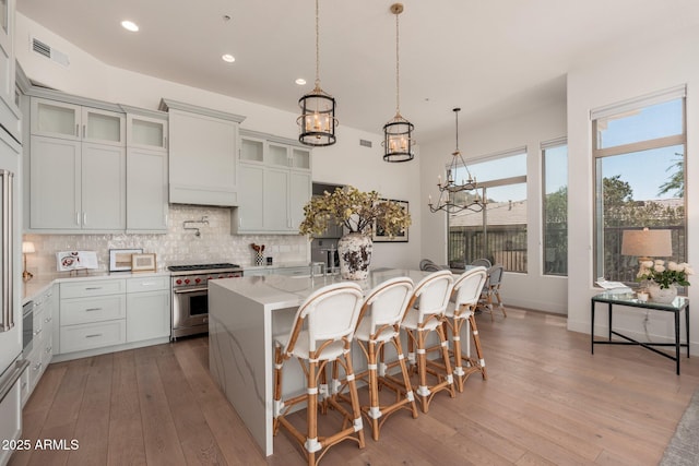 kitchen featuring high end range, recessed lighting, an island with sink, backsplash, and light wood-type flooring