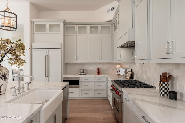 kitchen with premium appliances, light wood-type flooring, a sink, decorative light fixtures, and tasteful backsplash