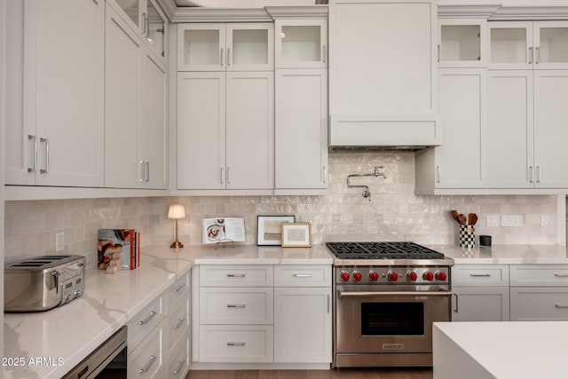 kitchen featuring designer stove, backsplash, light stone counters, and white cabinetry