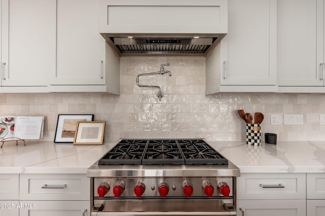 kitchen featuring high end stove, decorative backsplash, white cabinets, custom exhaust hood, and light stone countertops