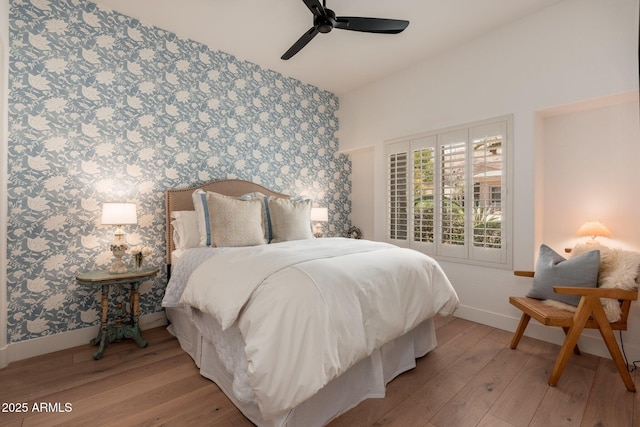 bedroom featuring wallpapered walls, an accent wall, baseboards, light wood finished floors, and a ceiling fan