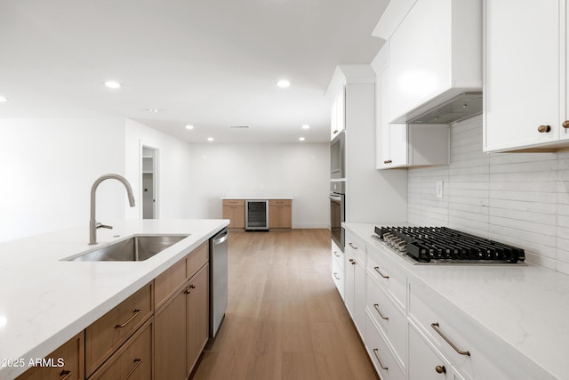 kitchen with wall chimney range hood, a sink, beverage cooler, appliances with stainless steel finishes, and tasteful backsplash