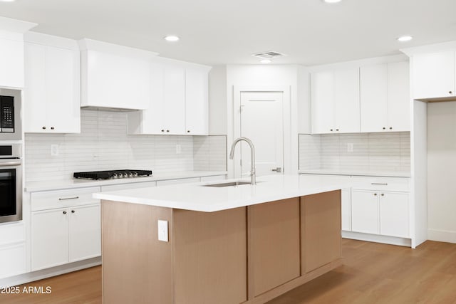 kitchen featuring a sink, gas cooktop, light countertops, light wood-type flooring, and recessed lighting