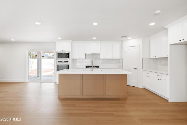 kitchen featuring stainless steel appliances, light countertops, decorative backsplash, recessed lighting, and light wood-type flooring