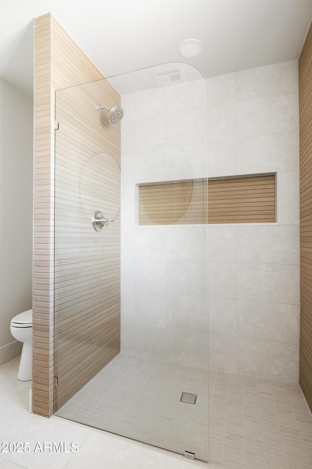 bathroom featuring a tile shower, toilet, and tile patterned floors