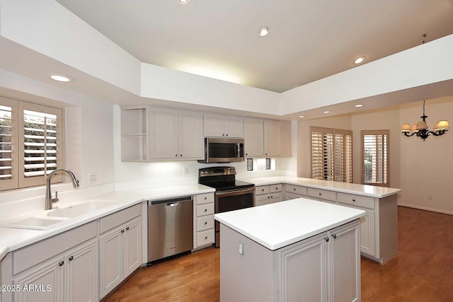 kitchen with a kitchen island, appliances with stainless steel finishes, sink, hanging light fixtures, and kitchen peninsula