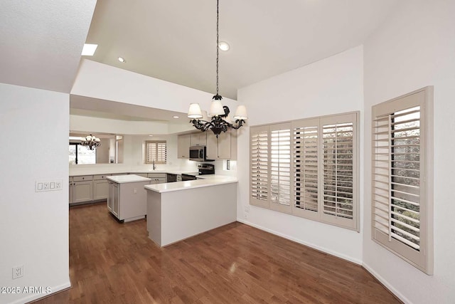 kitchen with pendant lighting, dark hardwood / wood-style flooring, a chandelier, kitchen peninsula, and stainless steel appliances