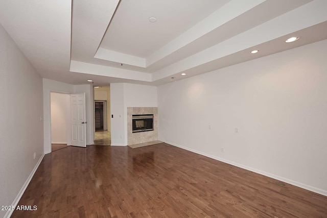 unfurnished living room with a raised ceiling, a tiled fireplace, and dark wood-type flooring