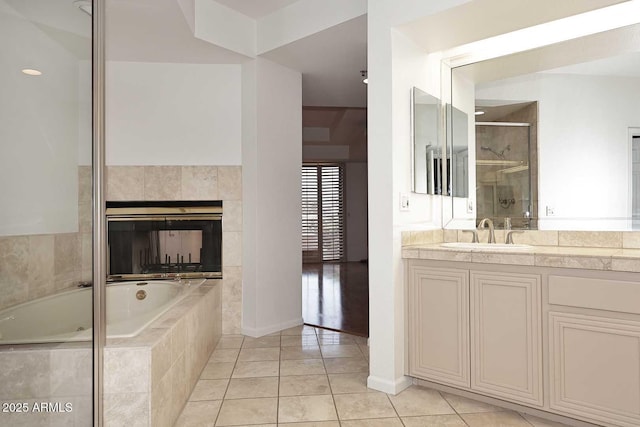 bathroom featuring a tiled fireplace, tiled tub, tile patterned flooring, and vanity