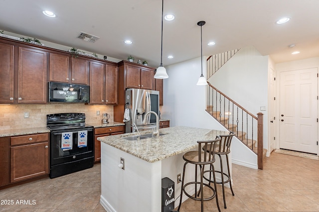 kitchen featuring visible vents, black appliances, a sink, a center island with sink, and backsplash