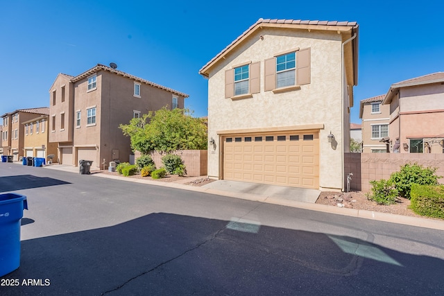 view of front of house with an attached garage, fence, a residential view, and stucco siding
