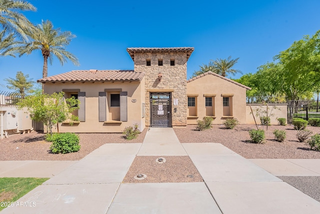 mediterranean / spanish house featuring stucco siding, stone siding, fence, and a tile roof