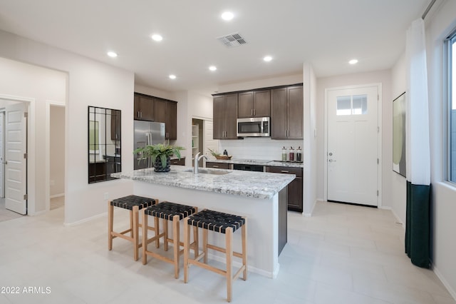 kitchen with visible vents, appliances with stainless steel finishes, a kitchen breakfast bar, dark brown cabinets, and a sink