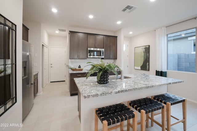 kitchen featuring visible vents, an island with sink, stainless steel appliances, dark brown cabinets, and a sink