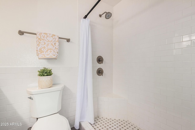 full bath with toilet, a stall shower, and wainscoting