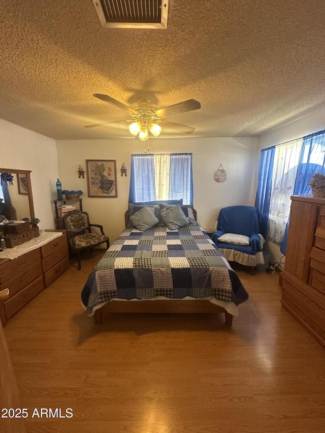 bedroom featuring ceiling fan, visible vents, multiple windows, and wood finished floors