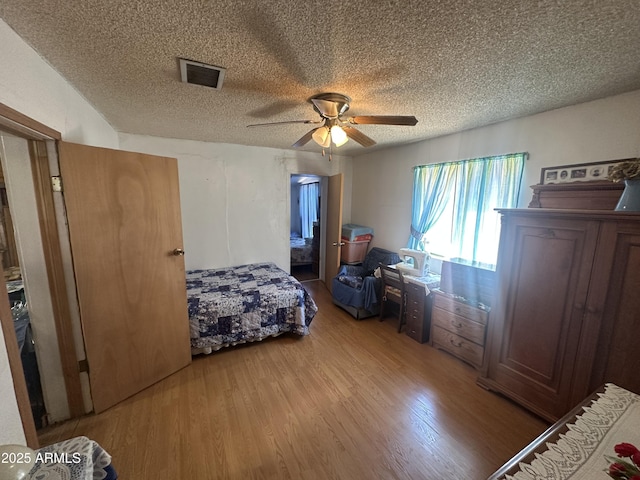 bedroom with ceiling fan, visible vents, a textured ceiling, and wood finished floors