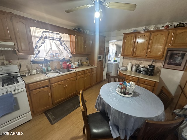 kitchen with white gas stove, a sink, light countertops, light wood-style floors, and under cabinet range hood