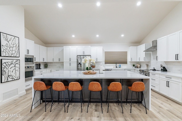 kitchen featuring appliances with stainless steel finishes, backsplash, a kitchen breakfast bar, wall chimney exhaust hood, and a spacious island