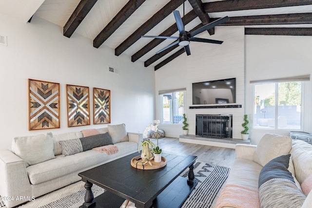 living room featuring hardwood / wood-style floors, high vaulted ceiling, ceiling fan, beam ceiling, and a large fireplace