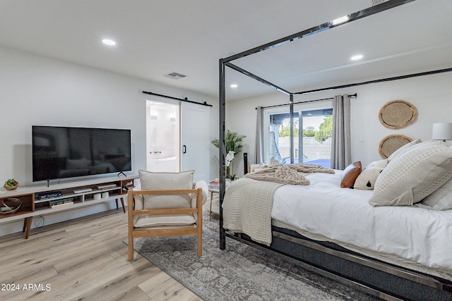 bedroom featuring a barn door, light hardwood / wood-style floors, and access to outside