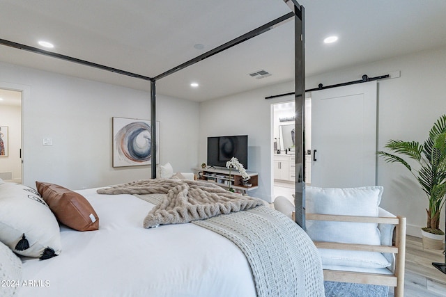 bedroom featuring light wood-type flooring, ensuite bath, and a barn door