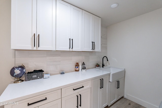 interior space featuring light hardwood / wood-style flooring, white cabinetry, tasteful backsplash, and sink