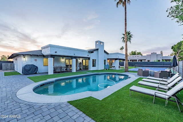 pool at dusk with a yard, an outdoor living space, a patio area, and a grill