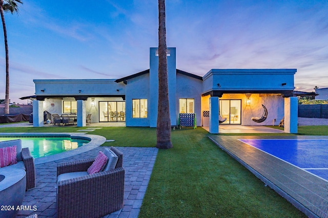 back house at dusk featuring a lawn and a patio area