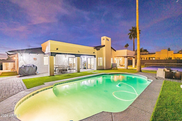 pool at dusk with a patio area and grilling area