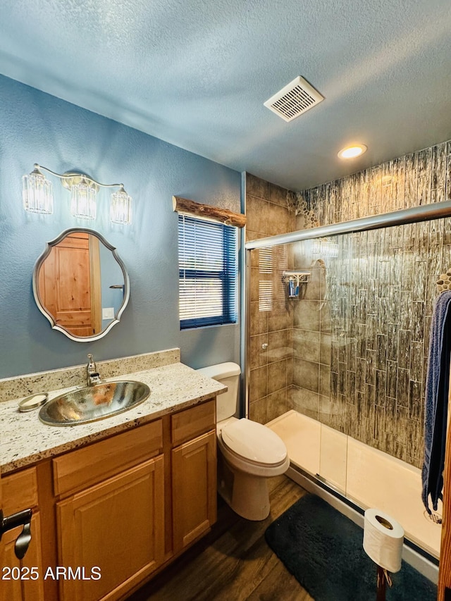 bathroom featuring wood finished floors, visible vents, a shower stall, a textured ceiling, and toilet