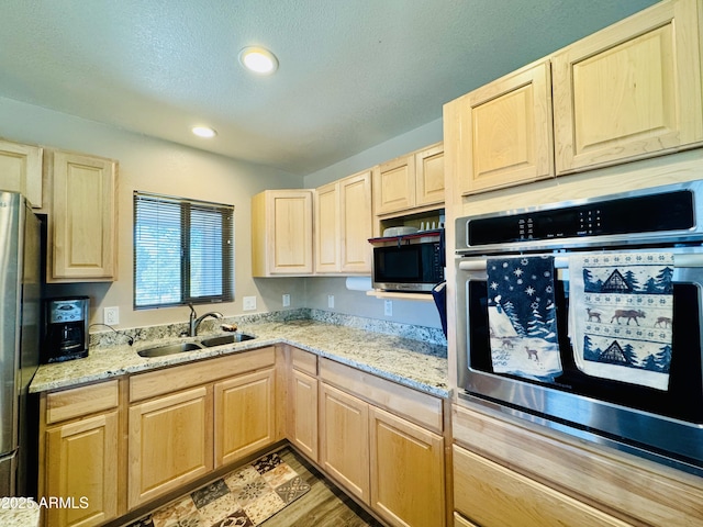 kitchen featuring light brown cabinets, light stone counters, recessed lighting, appliances with stainless steel finishes, and a sink