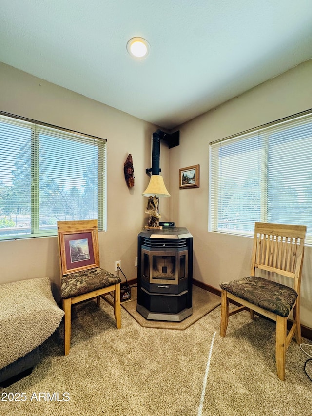 sitting room with baseboards, a wood stove, and carpet