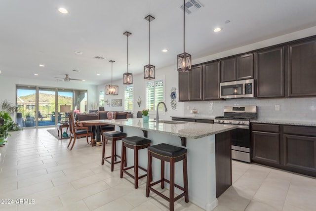 kitchen featuring light stone counters, appliances with stainless steel finishes, pendant lighting, sink, and a kitchen island with sink