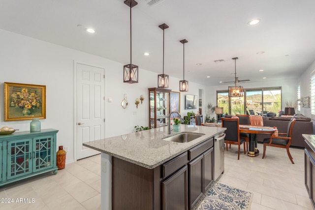 kitchen featuring light stone counters, dark brown cabinets, hanging light fixtures, sink, and a kitchen island with sink