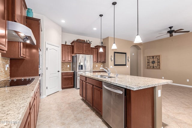 kitchen with appliances with stainless steel finishes, wall chimney exhaust hood, a center island with sink, tasteful backsplash, and sink