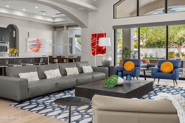 living room with recessed lighting, arched walkways, a towering ceiling, and wood finished floors