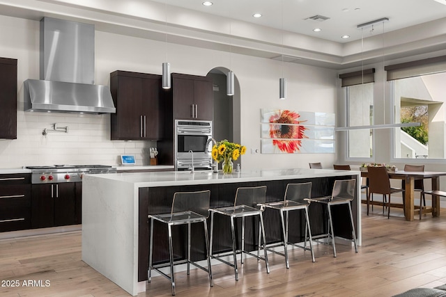 kitchen with light countertops, wall chimney range hood, an island with sink, and a breakfast bar