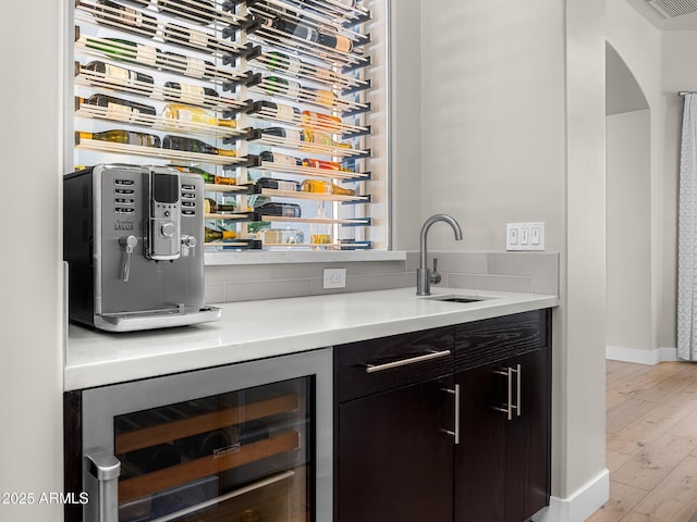 bar featuring light wood finished floors, beverage cooler, baseboards, arched walkways, and a sink