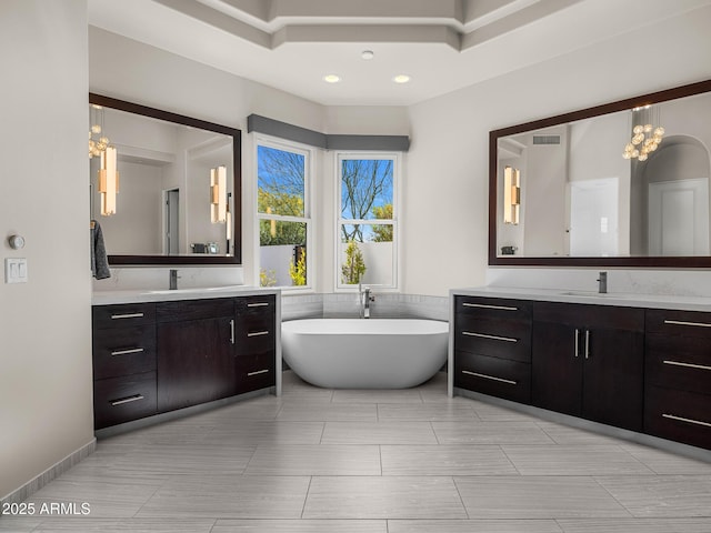 full bathroom with two vanities, a freestanding bath, visible vents, and a sink