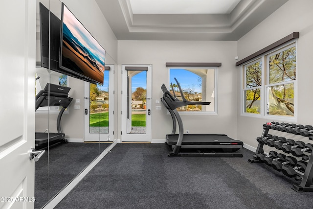 workout room featuring a raised ceiling, a wealth of natural light, and baseboards